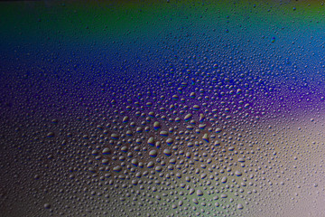 Water drops on glass with colorful rainbow background. Morning dew on the window with a refractive reflection of multicolored sunlight.