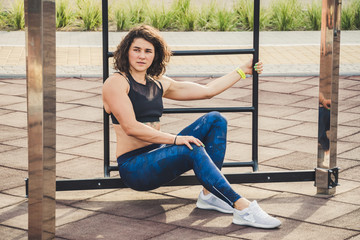 Attractive fit young woman in sport wear rest on the street workout area. The healthy lifestyle in the city. Street portrait strong woman poses at gym. Beautiful athletic woman in sports bra posing