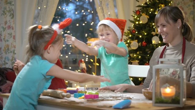 Children with their mom making gingerbread cookies for family dinner on Christmas eve. Kids laughing and fooling around and throwing flour at each other