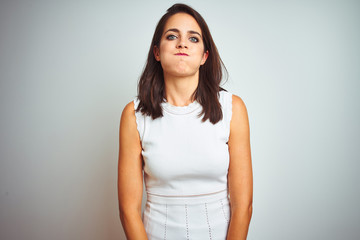 Young beautiful woman wearing dress standing over white isolated background puffing cheeks with funny face. Mouth inflated with air, crazy expression.