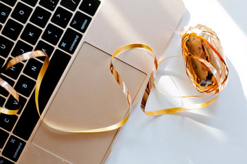 Gold wrapping ribbon on a table near the keyboard of laptop, top view. Shopping online