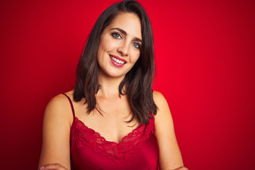 Naklejka premium Young beautiful woman wearing sexy lingerie over red isolated background happy face smiling with crossed arms looking at the camera. Positive person.