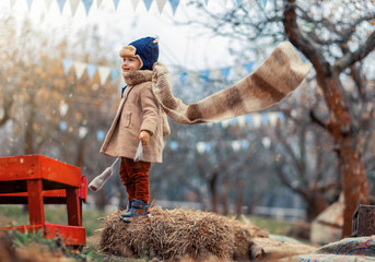 Cute little kid having enjoying countryside. Baby boy playing outdoors, scarf in air autumn time