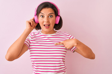 Young beautiful woman listening to music using headphones over isolated pink background with surprise face pointing finger to himself