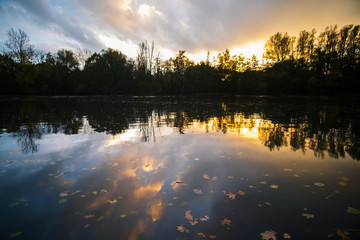 Sunset behind a small lake with pretty reflections and autumn leaves in the water