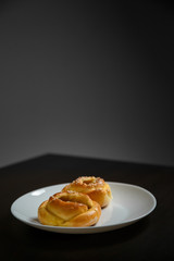 Vertical shot of delicious sesame buns or pies on white plate on black wooden table background. Tasty unhealthy snack for lunch. Overweight, diet, nutrition, eating habits concept. Copy space.