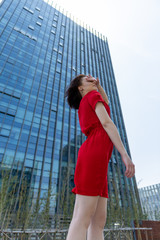 Fototapeta na wymiar young woman dancing in red dress near office building