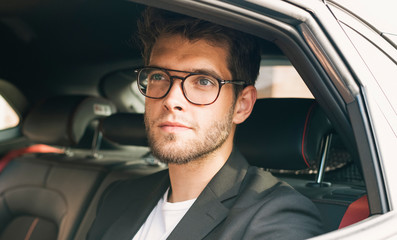 Young and attractive man with a beard and glasses smiles inside a car. Business