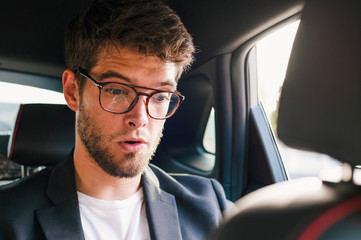 Young and attractive man with a beard and glasses smiles inside a car. BusinessYoung and attractive man with a beard and glasses with a surprised face is inside a car. Business