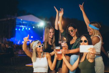Female friends taking selfie wile cheering with beer at the festival