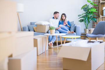 Young beautiful couple sitting on the sofa at new home around cardboard boxes
