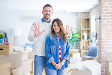 Young beautiful couple standing at new home around cardboard boxes showing and pointing up with fingers number nine while smiling confident and happy.