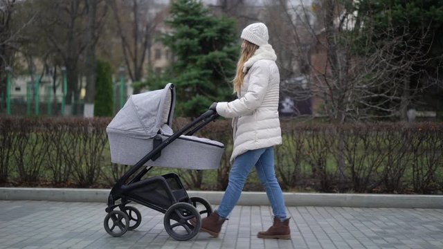 Young mother walking with a child in pram. Autumn season