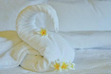 Fototapeta na wymiar Beautiful swan from white bath towel decorate on white bed. towel swan with topical flowers - frangipani. Nice greeting from Hotel.