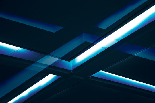 Cross of lighting fixtures on dropped or suspension ceiling. Abstract modern architecture. Office building interior with daylight luminescent lamps. Background of blue structure glowing in darkness.
