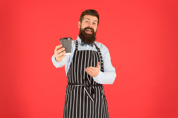 this is for you. bearded man hold take away coffee. brutal waiter in cafe. mature man red background. skilled servant. barista hipster chef apron. elegant confident bartender. male drink coffee