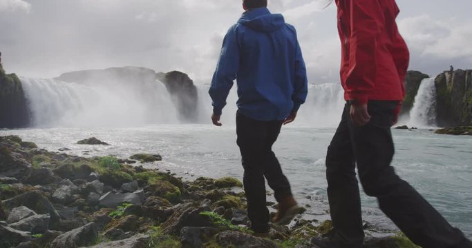 Iceland Travel Couple hiking in nature on Iceland on hike by waterfall Godafoss. People enjoying outdoor active healthy lifestyle on travel visiting landmarks in Icelandic nature. RED Cinema Camera.