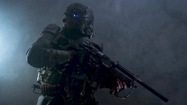 Post apocalyptic warrior in full protective gear is aiming from his weapon at dark room.