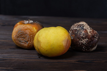 on a wooden table are fruits. in the foreground is a ripe green apple, behind it are black and brown rotten apples, covered with mold and fungi. focus on a ripe apple. concept art rotting process