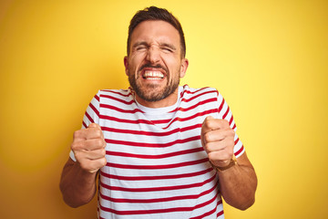 Young handsome man wearing casual red striped t-shirt over yellow isolated background excited for success with arms raised and eyes closed celebrating victory smiling. Winner concept.