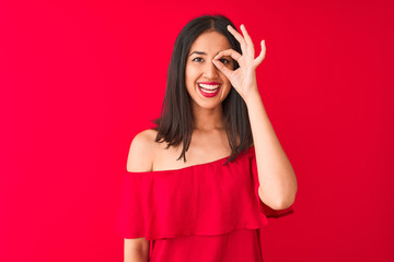 Young beautiful chinese woman wearing casual t-shirt standing over isolated red background doing ok gesture with hand smiling, eye looking through fingers with happy face.