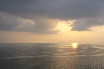 Morning sunrise with penetrating sun rays through black rain storm clouds over the ocean sea