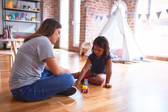 Beautiful teacher and toddler girl playing with train at kindergarten
