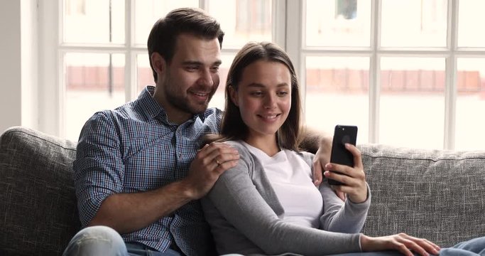 Happy young couple using smartphone social media apps at home