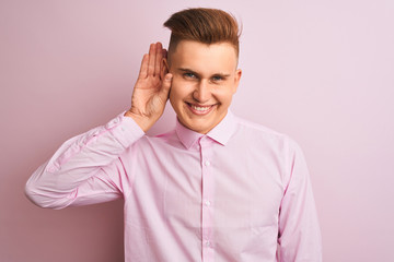 Young handsome businessman wearing elegant shirt standing over isolated pink background smiling with hand over ear listening an hearing to rumor or gossip. Deafness concept.