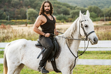 Young jockey training his horse for a ride. Good looking, hunky cowboy rides horse at beautiful...
