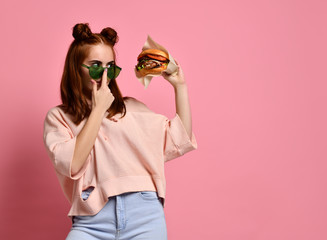 Beautiful teenage girl with red hair holding burger and beverage in hand. Ginger student girl has...