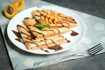Crepes with chocolate sauce, fruits and mint on a dark background.