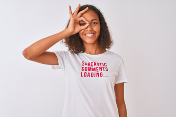 Brazilian woman wearing fanny t-shirt with irony comments over isolated white background with happy face smiling doing ok sign with hand on eye looking through fingers