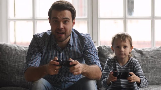 Happy dad and son holding joysticks playing videogame on sofa