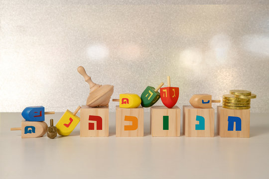 concept of of jewish religious holiday hanukkah with wooden spinning top toy (dreidel), wooden cubes saying "hanukkah" in hebrew and chocolate coins