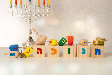 concept of of jewish religious holiday hanukkah with hanukkah chandellier (menorah) wooden spinning top toys (dreidel), cubes saying "hanukkah" in hebrew and chocolate coins