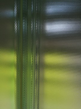 Rippled glass blocks. Close-up of modern architecture or interior design. Semitransparent backlit wall or window.  Crystal mosaic pattern of material or technology background in green and yellow color