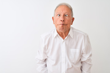 Senior grey-haired man wearing elegant shirt standing over isolated white background making fish face with lips, crazy and comical gesture. Funny expression.