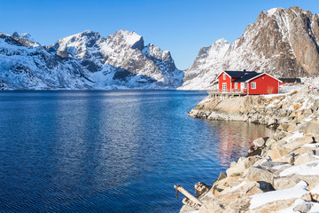 Rood vissershuis voor een besneeuwde bergketen op de Lofoten-eilanden in de winter