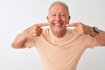 Senior grey-haired man wearing striped t-shirt standing over isolated white background smiling cheerful showing and pointing with fingers teeth and mouth. Dental health concept.