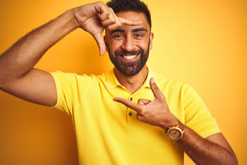 Young indian man wearing polo standing over isolated yellow background smiling making frame with...