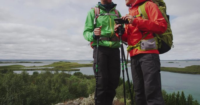 Couple hiking walking and taking phone selfie photo in nature. People on hike on travel walking with hiking poles in beautiful landscape. Lake Myvatn, Iceland. RED EPIC. TRACKING SHOT.