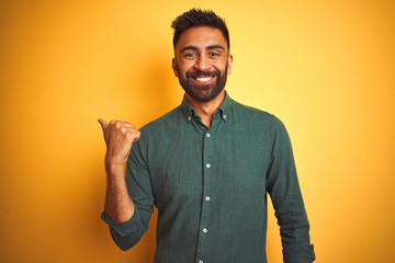 Young indian businessman wearing elegant shirt standing over isolated white background smiling with happy face looking and pointing to the side with thumb up.
