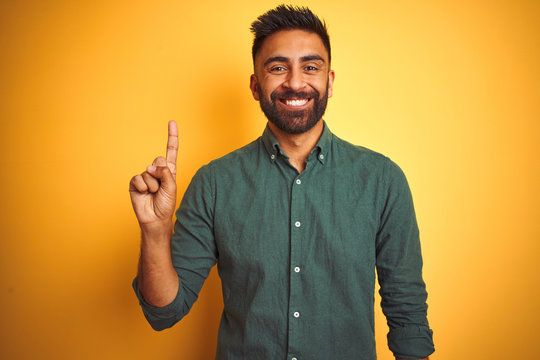 Young indian businessman wearing elegant shirt standing over isolated white background showing and pointing up with finger number one while smiling confident and happy.