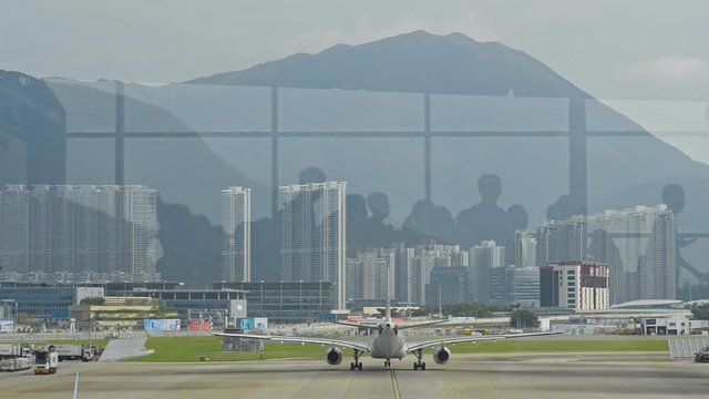 airplane takeoff view from hong kong international airport. walking people reflection. passengers in waiting room. urban building background. aircraft, runway, departure concept.