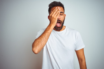 Young indian man wearing t-shirt standing over isolated white background Yawning tired covering...