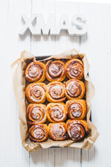 Cinnamon rolls with sugar icing  ready to be eaten for christmas holiday, top view over a rustic wooden  background  with a  giant xmas decoration of wooden atop, flat layout