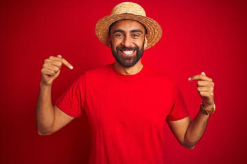 Young handsome indian man wearing t-shirt and hat over isolated red background looking confident...