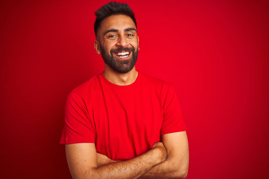 Young Handsome Indian Man Wearing T-shirt Over Isolated Red Background Happy Face Smiling With Crossed Arms Looking At The Camera. Positive Person.