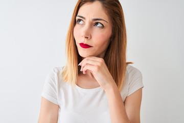 Beautiful redhead woman wearing casual t-shirt standing over isolated white background serious face thinking about question, very confused idea